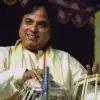 A tabla performer seated on stage, hands positioned on the drums, wearing a light-colored outfit.