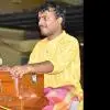 A male harmonium player in a yellow kurta performs on stage, seated behind a wooden harmonium with a microphone positioned in front, during a live Indian classical music concert.