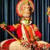 Kathakali artist Jadav Das performing on stage in traditional costume, elaborate headgear, and green facial makeup during a classical Kathakali dance performance.