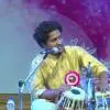 Tabla player Jagmitra Lingade performing on stage, seated with the instrument and playing while positioned near a microphone during a live concert.