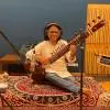 Sitar player Ravi Chary seated in a recording studio, playing the instrument with microphones set up around him and wearing headphones.