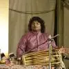 Pakhawaj artist Rishi Shankar Upadhyay performing on stage, seated with the instrument and gesturing during a live classical music concert.