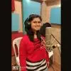 Singer Shalmali Sukthankar recording vocals in a music studio while wearing headphones and standing in front of a microphone.