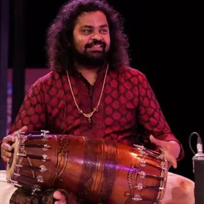 Patri Satish Kumar performing on stage, playing the mridangam during a concert.