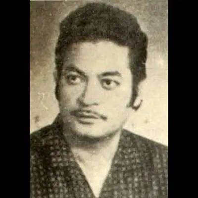 Black-and-white portrait of a young man with neatly styled hair and a thin moustache, looking directly at the camera with a composed expression. He is wearing a patterned traditional outfit, and the image has a vintage, archival quality.