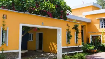 A yellow building with a courtyard entrance, surrounded by greenery and flowering plants.