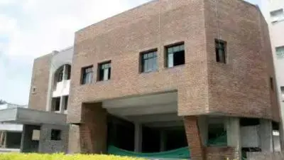 Exterior view of MES Balshikshan Auditorium in Kothrud, Pune, a brick-clad modern building with rectangular windows and an open ground-level entrance area surrounded by greenery.