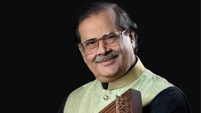 Portrait of Hindustani classical vocalist Pandit Ajoy Chakrabarty holding a swar mandal against a black background.