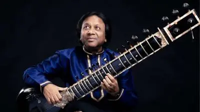 Hindustani classical sitar maestro Ustad Shahid Parvez Khan seated with his sitar during a performance, wearing a blue kurta against a dark background.
