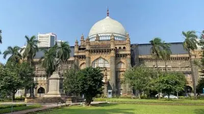 Exterior view of the Chhatrapati Shivaji Maharaj Vastu Sangrahalaya in Mumbai featuring Indo-Saracenic architecture, a large central dome, palm trees and landscaped gardens in the foreground.