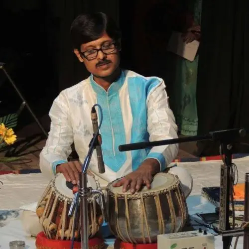 Tabla player performing on stage, seated with microphones and traditional attire.