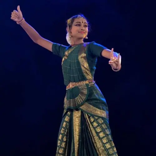 Classical dancer Janani Murali performing Bharatanatyam on stage in a traditional green costume and jewellery.