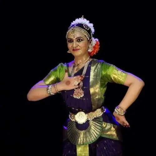Bharatanatyam dancer performing in a classical pose, wearing traditional costume and temple jewellery against a black background.