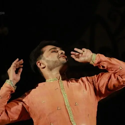 Kathak dancer Souvik Chakraborty performing on stage in an orange traditional costume, captured in a graceful pose during a classical Indian dance performance.
