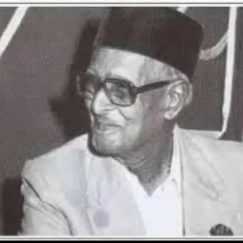 Black and white portrait of Pandit Wamanrao Sadolikar wearing a traditional cap and glasses, seated and looking to the side.