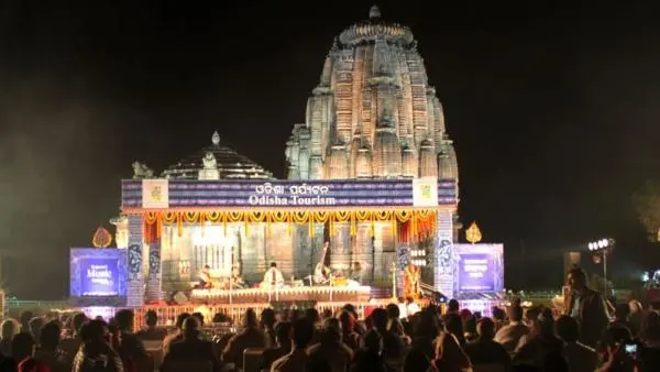 Audience gathered for a classical music performance at the Rajarani Music Festival, with illuminated temple architecture and Odisha Tourism branding in the background at night.