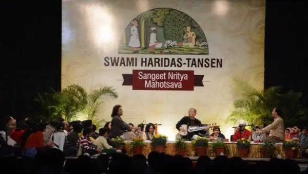 Classical music performance at the Swami Haridas-Tansen Sangeet Nritya Mahotsava featuring musicians performing on stage before a large festival backdrop and seated audience.