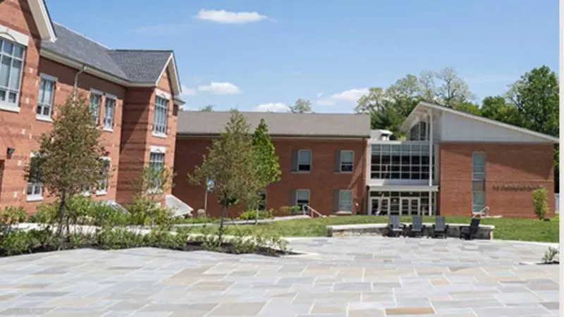 Exterior view of Langley High School Auditorium showing the red-brick school building, main entrance with glass facade, and open courtyard area under a clear sky.