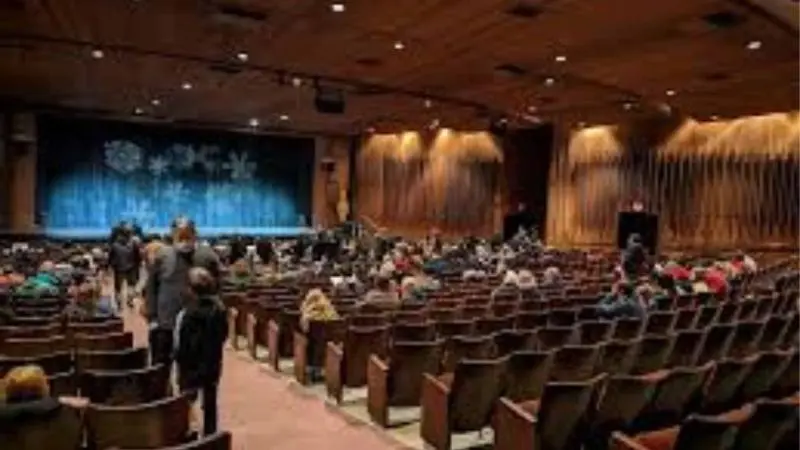Interior view of Smithwick Theatre auditorium with large seating area, wooden interiors, and stage with blue curtain before a live performance.