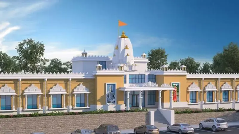 Exterior view of Chinmaya Amarnath in Pittsburgh, featuring a temple-style building with a central white dome and saffron flag, symmetrical façade with decorative columns and arches, and a parking area in front.