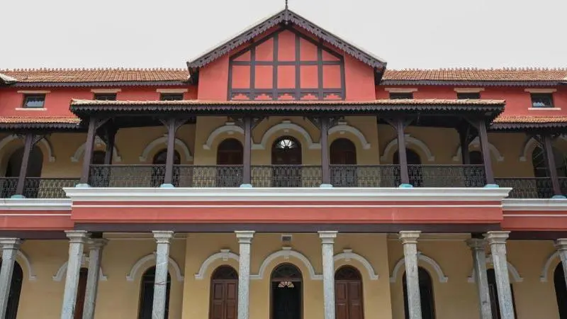 Front view of the historic Old Fort High School Grounds building featuring colonial-style architecture, arched corridors, tiled roofs and a symmetrical multi-storey facade.