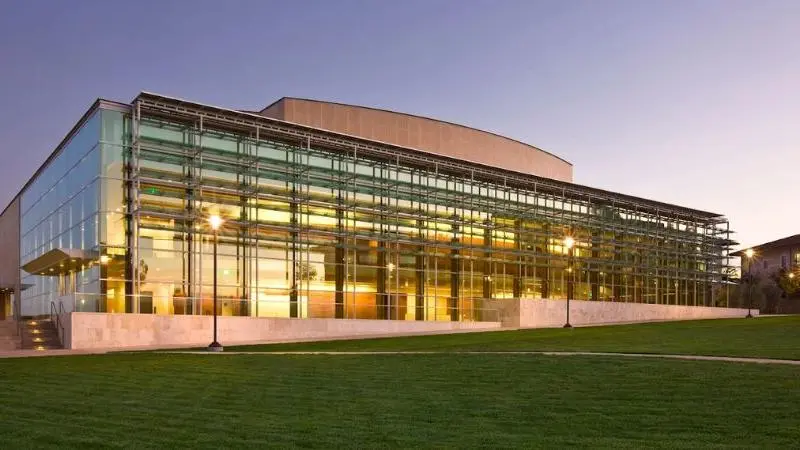Exterior view of the Soka Performing Arts Center featuring modern glass architecture illuminated at dusk with a landscaped lawn in the foreground.